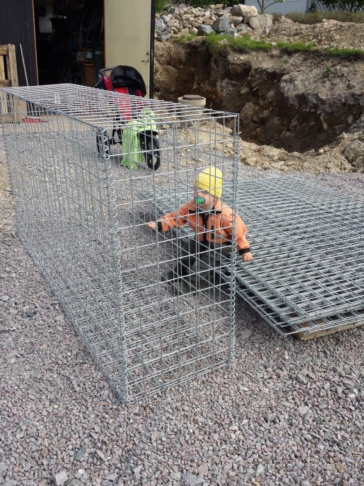 Tomma gabionkorgar installerade i trädgård för stödmur, med verktyg och byggmaterial i bakgrunden.