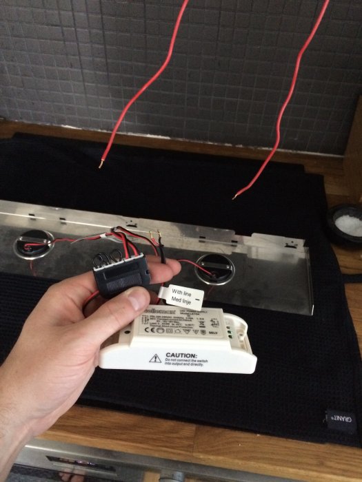 Hand håller en elektrisk strömbrytare över en öppen apparatlåda med lösa kablar och en varningsetikett.