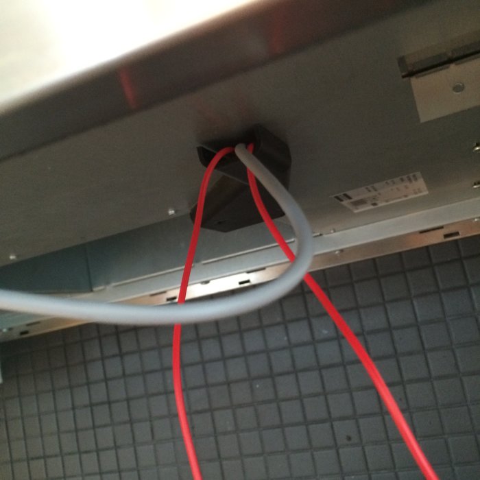 Elektriska anslutningar under en köksfläkt med röda kablar som illustrerar ett pågående byte från halogen till LED-belysning.
