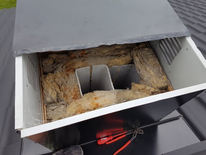 Takhuven öppnad som visar isolerade avluftningsrör med kondens, omgivna av glasull, på ett plattak.