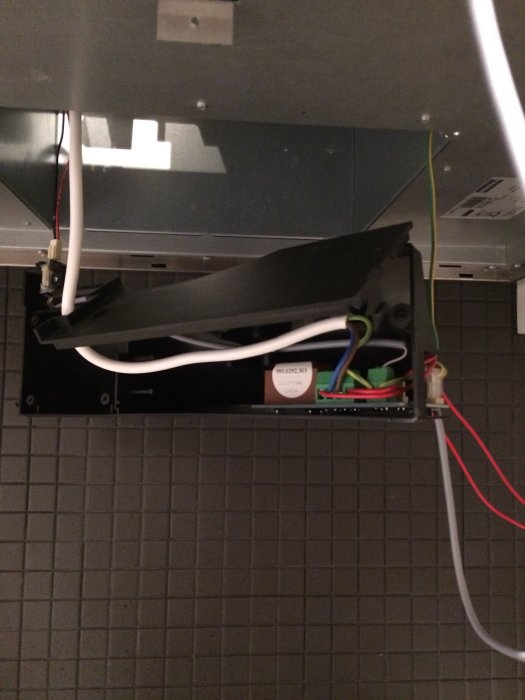 Bakom elektronikknappar avtäckt svart plastbox med kablar och komponenter på en vägg.