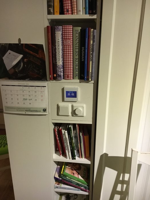 Nya lampknappar och en bluetooth stereo installerade på en vägg bredvid en bokhylla med kokböcker och en kalender.