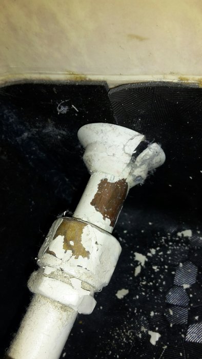 En närbild av en kopparvattenledning med en vinkelkoppling och flagnande vit färg.