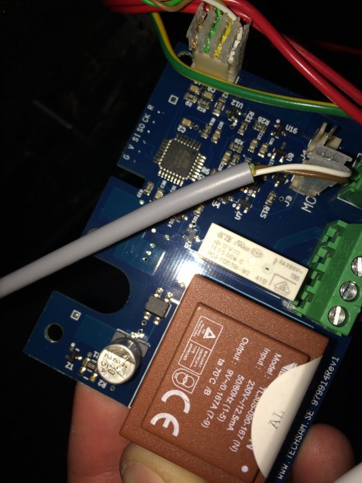 Hand håller ett kretskort med elektroniska komponenter och kondensator nära en vit klump som antyds vara föremål för byte.