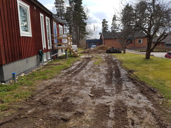 Lerig uppdykt gräsmatta vid ett rött trähus signalerar starten på ett bygg- eller trädgårdsprojekt.