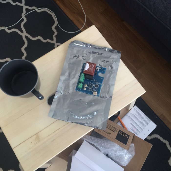 Elektronisk kretsplatta på bord med kaffekopp, förpackningsmaterial och andra objekt.