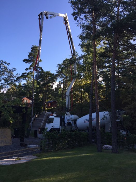 En betongbil och pumpbil gjuter betong för att anlägga gångar i en trädgård.