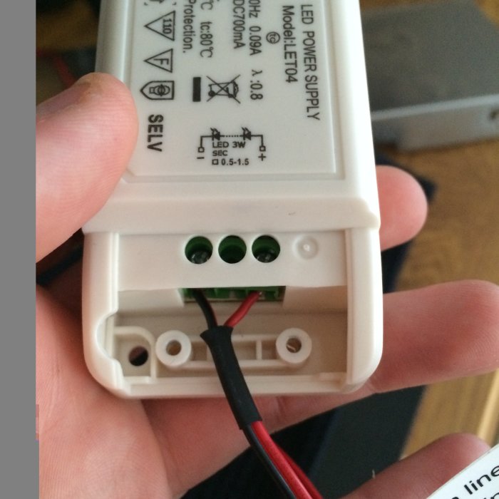 Närbild på en hand som håller en LED-driver med inkopplade kablar redo för att anslutas till ström.