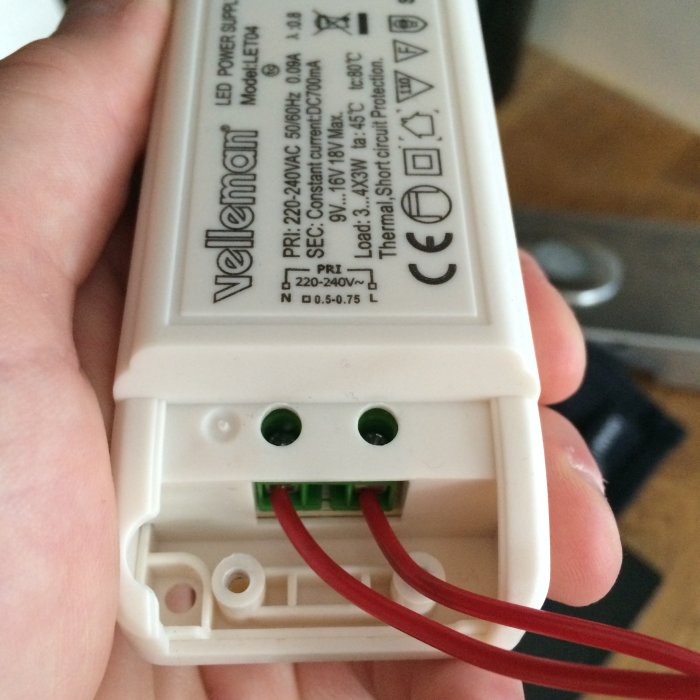 Hand håller ett Velleman LED-drivdon med korrekt inkopplade röda kablar i väntan på godkännande.