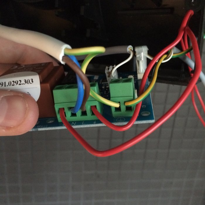 Närbild av elektriska kablar kopplade till en kretskortsanslutning med en hand som håller en kabel.