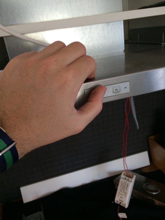 Hand trycker på en knapp för köksfläkt, med synlig elanslutning och etikett på ledningar.