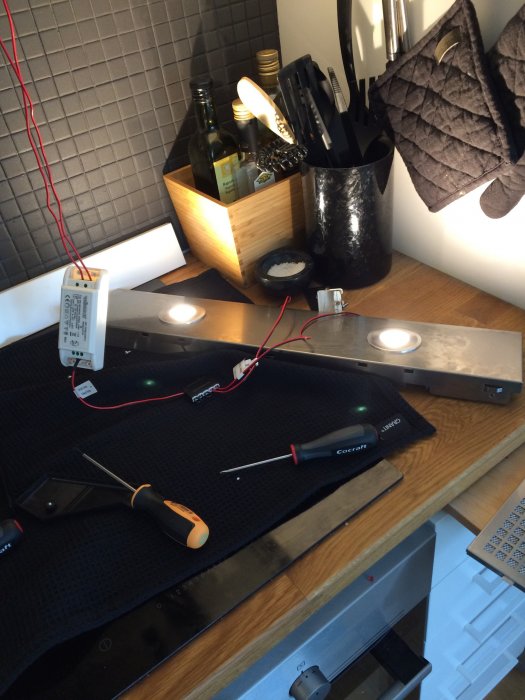 Installation av köksbelysning med ledningar, skruvmejslar och köksredskap på bänkskiva.