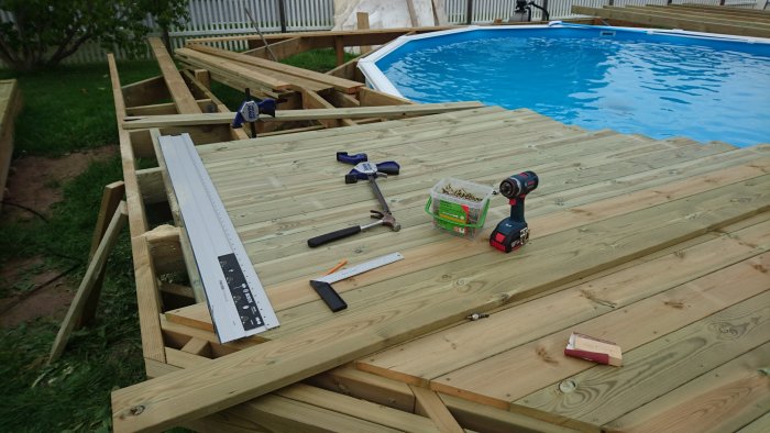 Halvt färdigt trädäck med verktyg framför poolen, under byggnation.