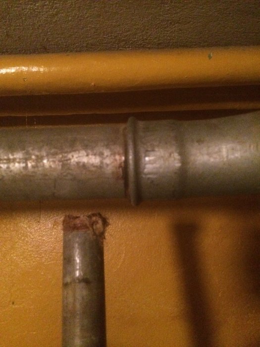 Utsnitt av två metallrör framför en gul vägg, det övre med en koppling, det undre avskuret, för diskussion om påfyllning av oljetank.
