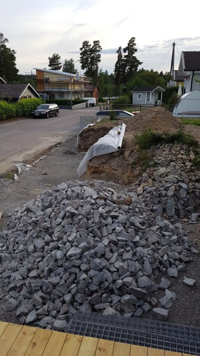 En hög med gabionsten på uppfarten och utförda grävarbeten i förgrunden med bostadsbyggen i bakgrunden.