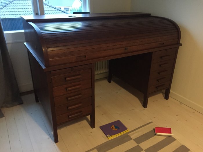 Renoverad äldre skrivbordsmöbel i teak med uppslaget lock och synliga åtgärder på lacken.