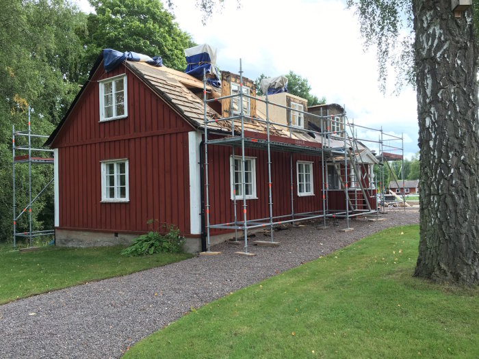 Renoveringsarbete på rött trähus med delvis avlägsnat tak och uppställt byggställning.