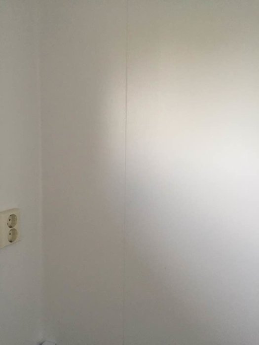 En suddig bild av en vit vägg med en synlig skarv och en eluttag på ena sidan.