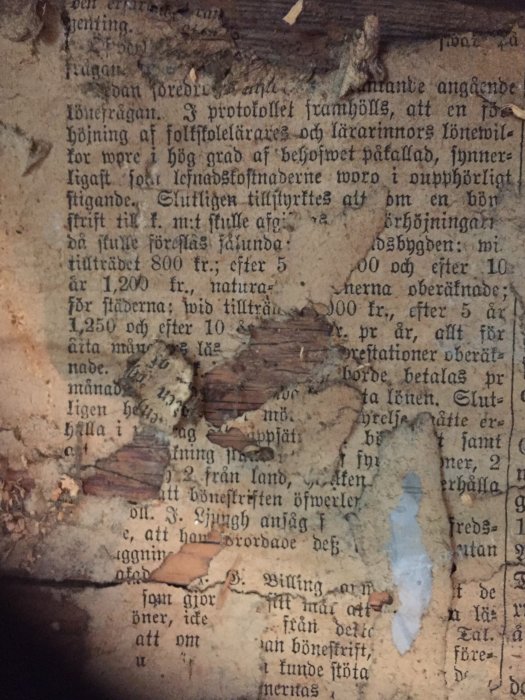 Gammal tidning inkapslad i vägg med synliga svenska textfragment och slitage.