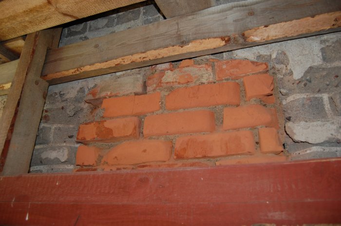 Närbild av en delvis återuppbyggd tegelvägg med nya tegelstenar bland äldre, slitna stenar och cement.