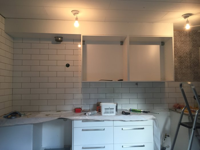 Enkla träramar fästa på en vägg med vit metrokakel ovanför ett köksarbetsbord i en byggprocess.