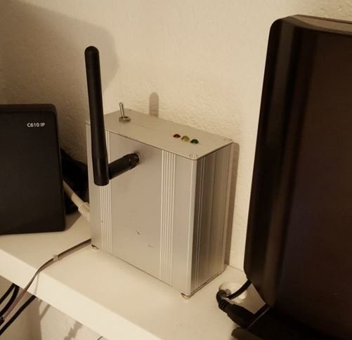 Egenbyggd DIY gateway med en antenn och lysdioder i ett metallhölje placerad bredvid andra nätverksenheter.