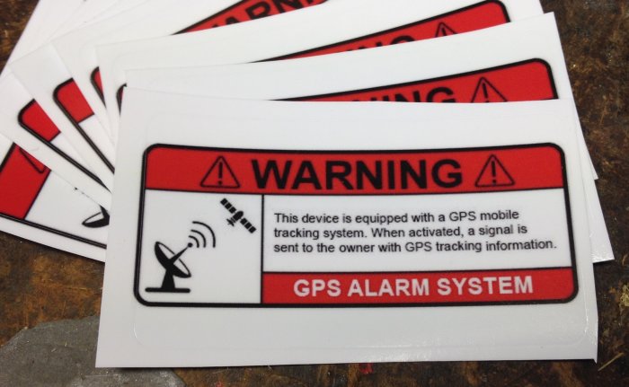 En hög med varningsklistermärken för GPS-alarmssystem på ett bord.