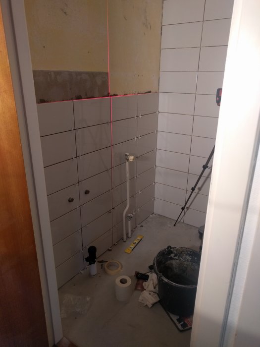 Kakelsättning i pågående badrumsrenovering med verktyg och byggmaterial synligt på golvet.