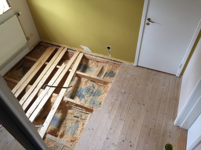 Renoverat golv med upprivna delar av trägolv och synliga reglar, fullt med sågspån och en kofot.