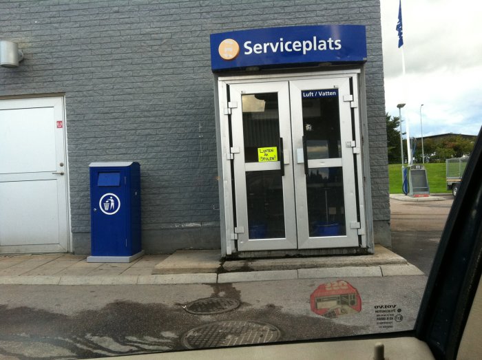 Serviceplatsbyggnad på tidigare Statoil station med en blå avfallskärl och skylten "Luft / Vatten".