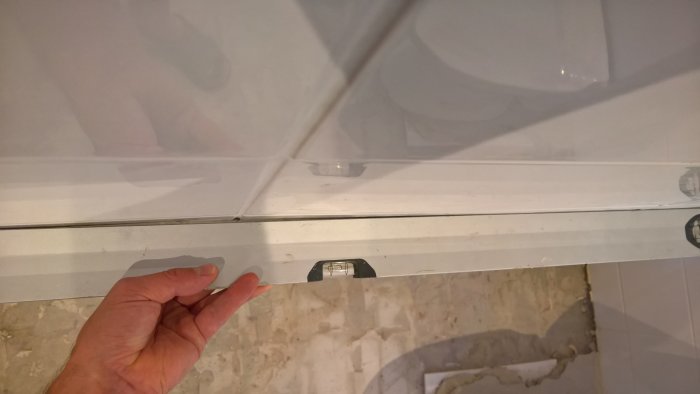 Hand pekar på bågnade kakelplattor vid badrumsdusch, dåligt lagda klinkerplattor på golvet syns.