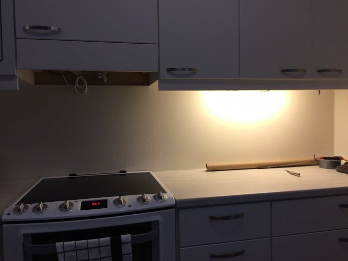 Kök under renovering med arbetsbänk, spishäll och öppna skåp utan frontpaneler.