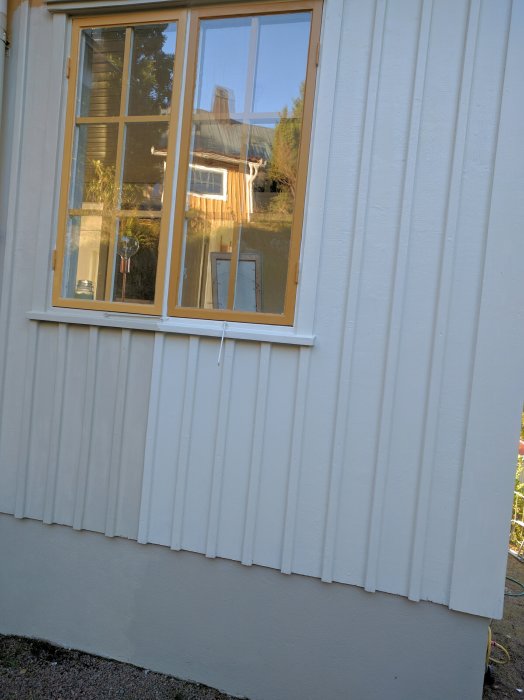Del av fasad på hus med vita plankor och fönster testmålat med beige färg.