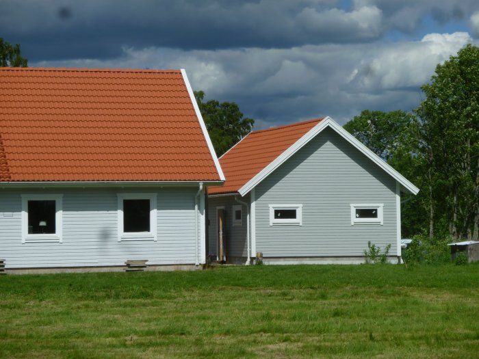 Hus och garage målade i olika nyanser av grått med tegelröda tak, omgivna av grönt gräs.