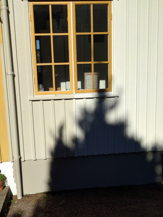 Vägg med fönster delvis i skugga som visar variationer i färgnyanser på träpanelen.