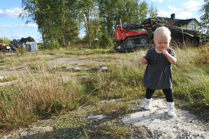 Barn på en avskalad tomt med byggmaskin i bakgrunden under markarbete.