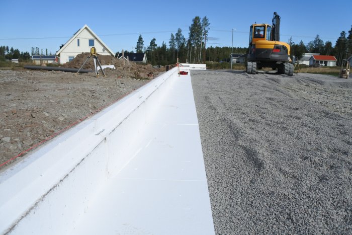 Grävmaskin och arbetsfordon vid en byggarbetsplats med nylagt kantblock och grusad mark.