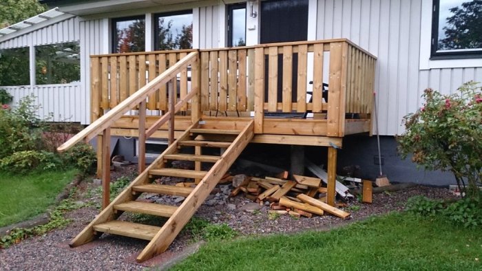 Nybyggd träaltan med trappa vid hus i 80-talsstil, gammal demonterad trappa i förgrunden.