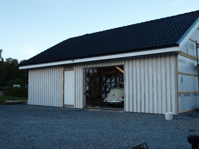 Nygrundad och delvis målad sidopanel på byggnad med öppna dörrar och skymt av bil inuti.