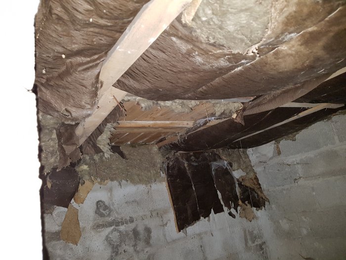 Skadad isolering i krypgrund med exponerade träbjälkar och sönderrivet svart material.