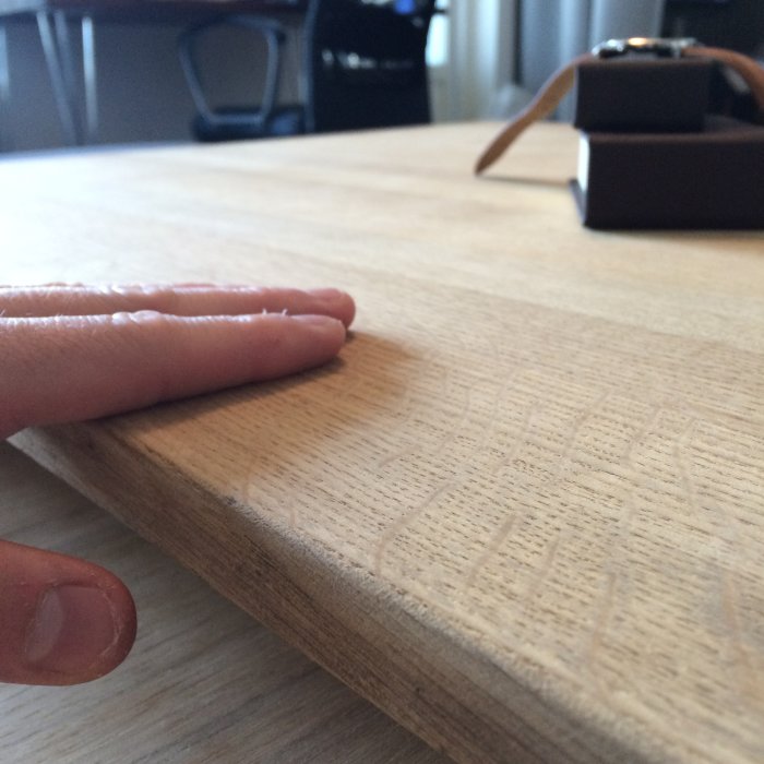 Närbild på en hand som rör vid ytan på ett nyslipat, obehandlat ek-soffbord.