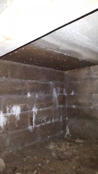 Fuktig krypgrund med betongbjälklag och murade väggar under entrétrappa, vita fläckar tyder på fukt.