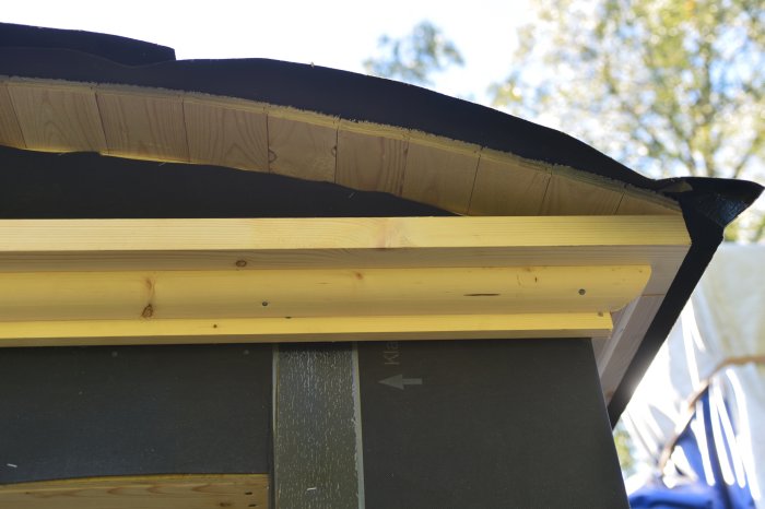 Detaljbild av en takkonstruktion med råspont, undertak och pågående listverksinstallation.
