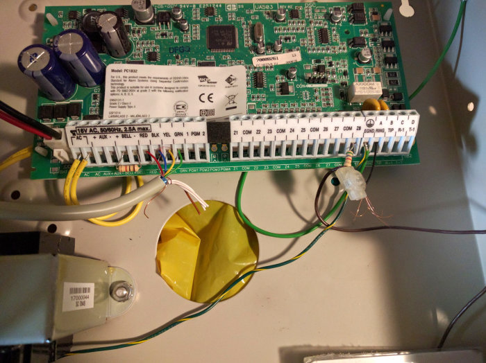 Öppen kretskortsbox med DSC PC1832 larmpanel, märkta kablar och osäker kabelanslutning.