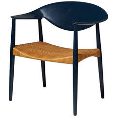 Designstol med mörkblått ryggstöd och sits i flätad rotting, mot vit bakgrund