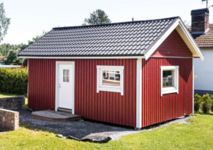 Röd stuga på ca 34 kvadratmeter med vita knutar och svart tak, ett fönster och dörr synlig.