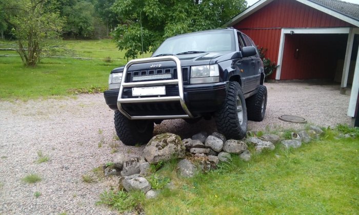 Jeep parkerad på stenig höjd framför röd byggnad, testar terrängkapacitet.