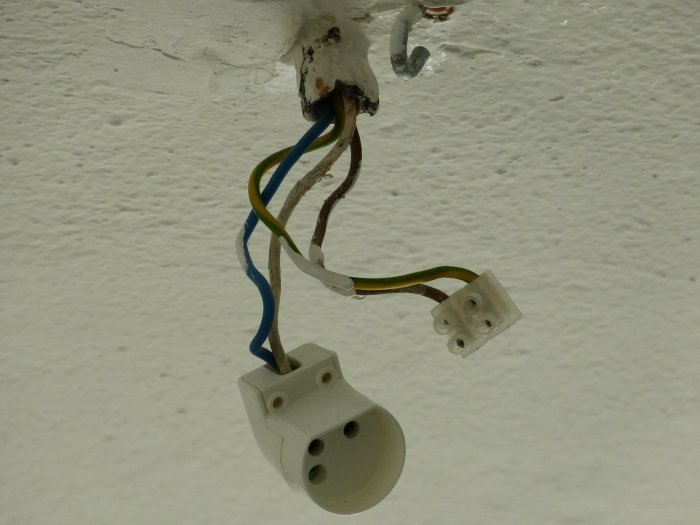 Ouppkopplad taklampa med synliga ledningar och en vit, omonterad elektrisk kontakt i taket.