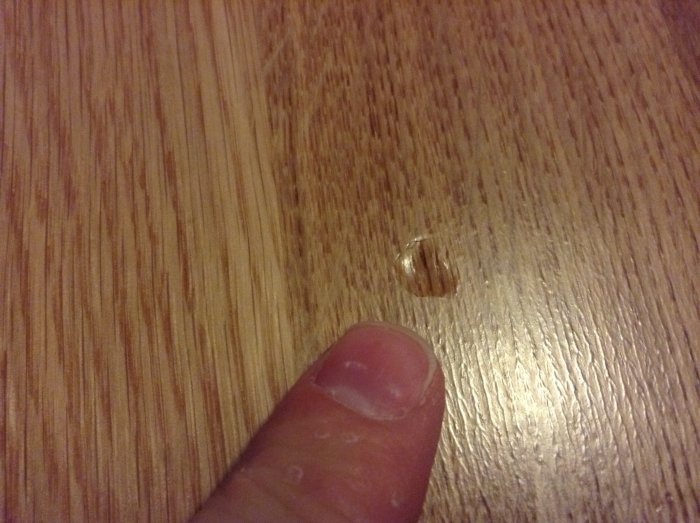 Skada på parkettgolv med ett finger som pekar på ett märke orsakat av en tappad brödkavel.