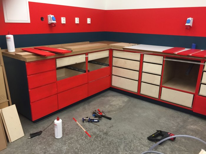 Röd och vit verkstadsinredning under montering med verktyg och material utspridda på golvet.